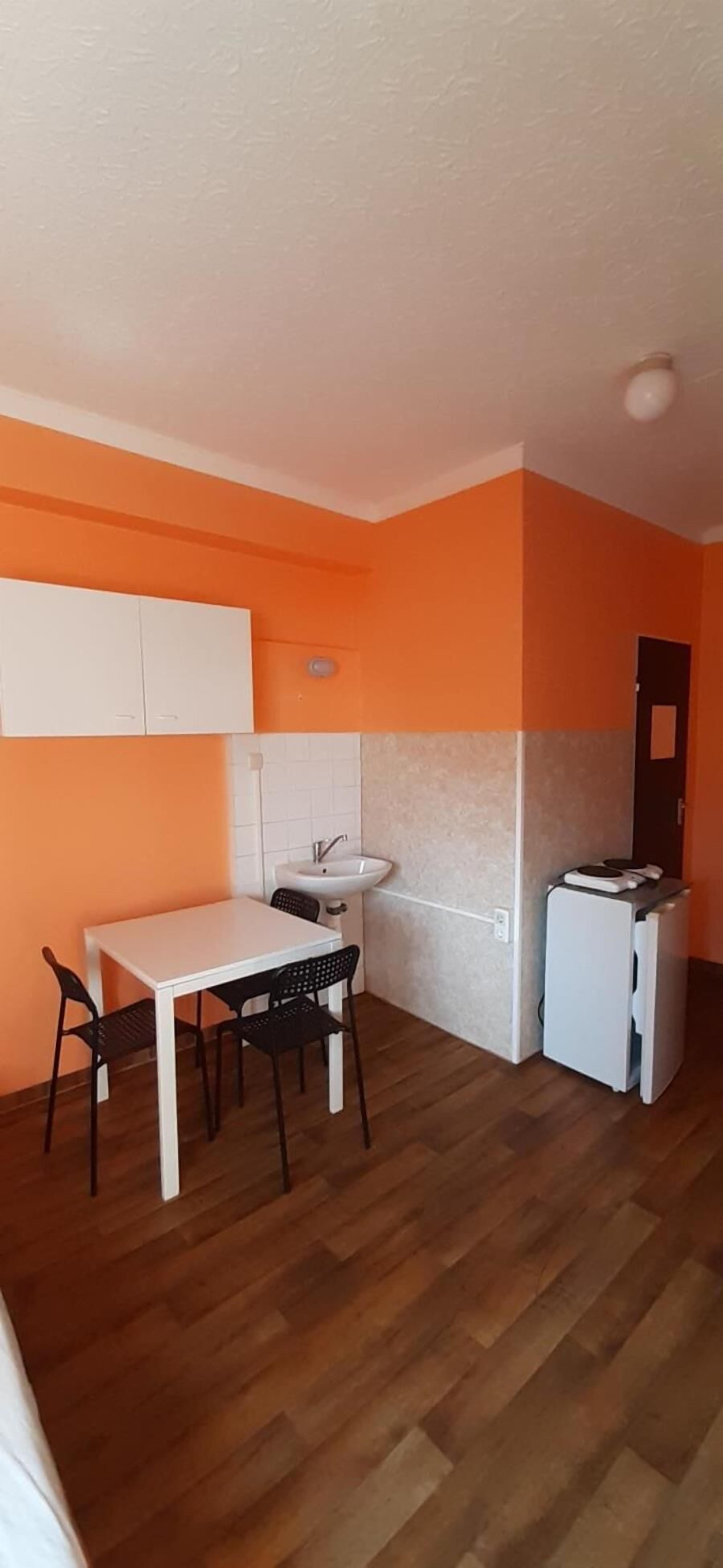 A compact kitchen with a white table and chairs, a sink, and a refrigerator.
