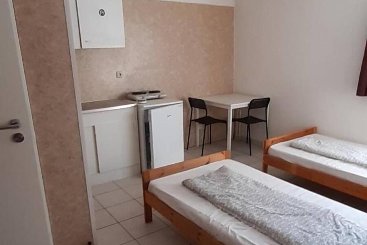 Une petite chambre propre, avec deux lits simples, un bureau, une chaise et un petit réfrigérateur.