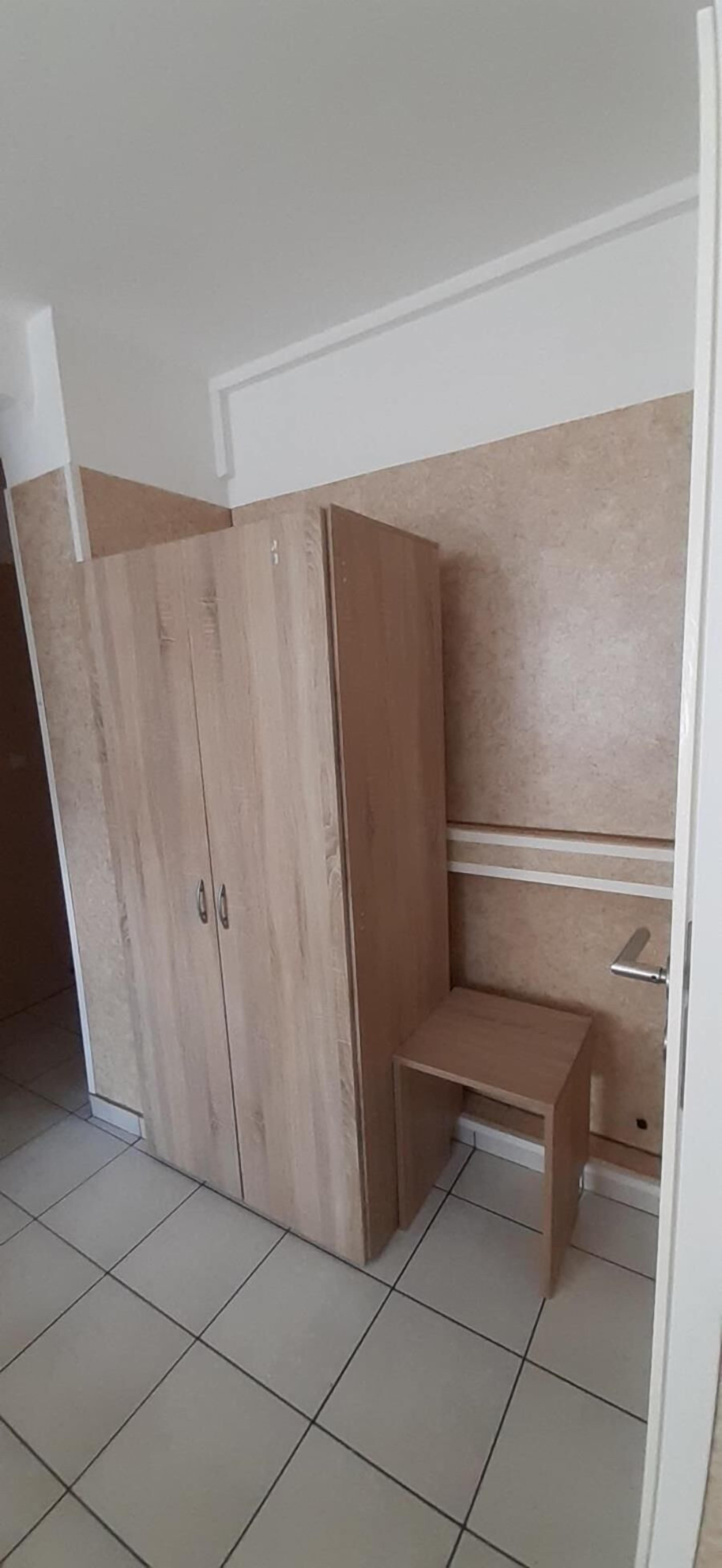 A room with a large wardrobe, a small wooden bench, and a tiled floor.