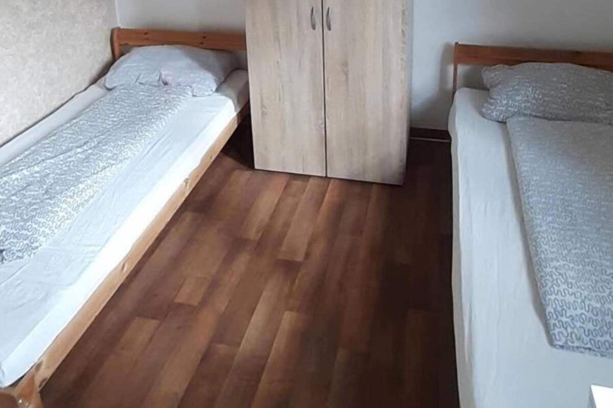 Une petite chambre avec deux lits simples, une armoire en bois et un bureau.