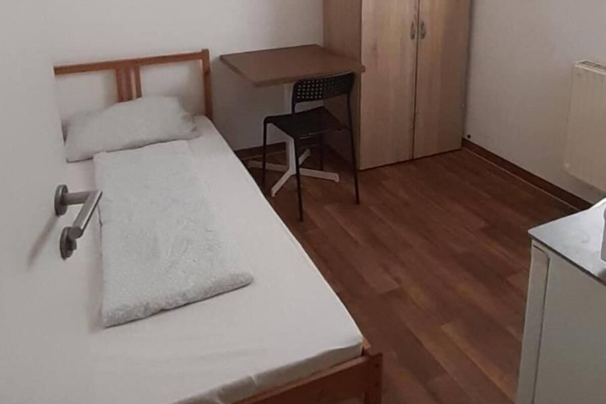 Une petite pièce propre, avec un lit, un bureau, une chaise et une armoire.