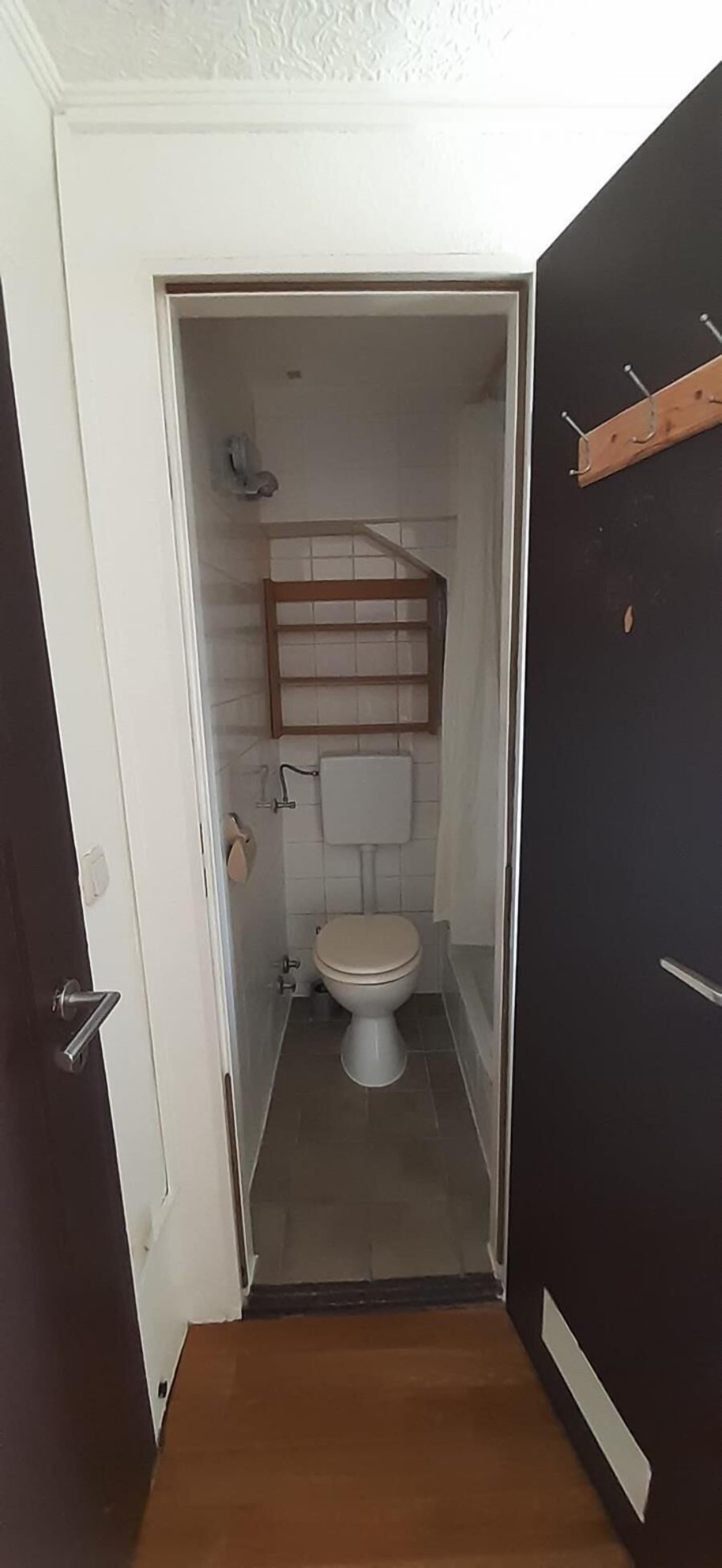 Un baño pequeño con inodoro, estante de madera y barra para toallas.
