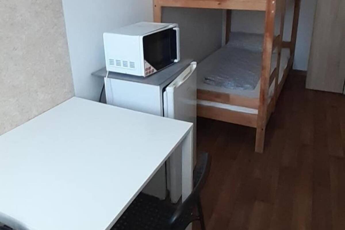 Une chambre avec un lit superposé, un bureau avec une chaise et un four à micro-ondes.