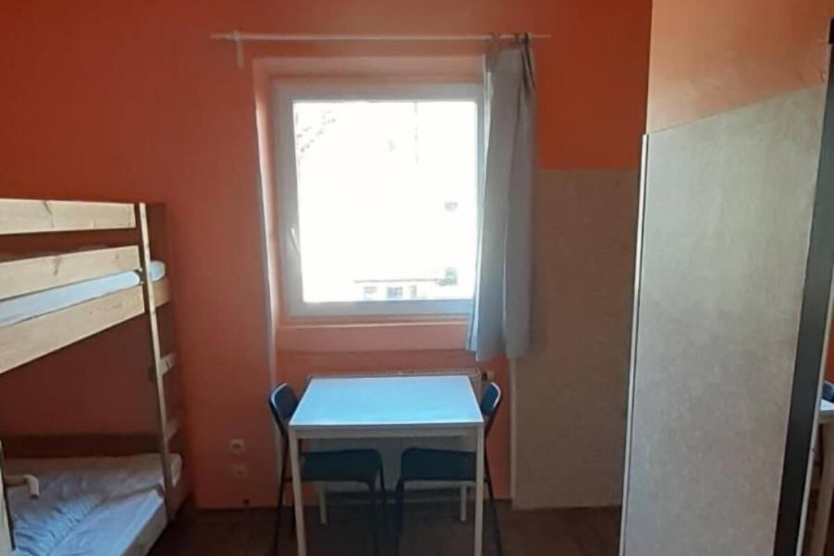 Une chambre avec un lit superposé, une table avec deux chaises, une fenêtre avec des rideaux et un ventilateur de plafond.