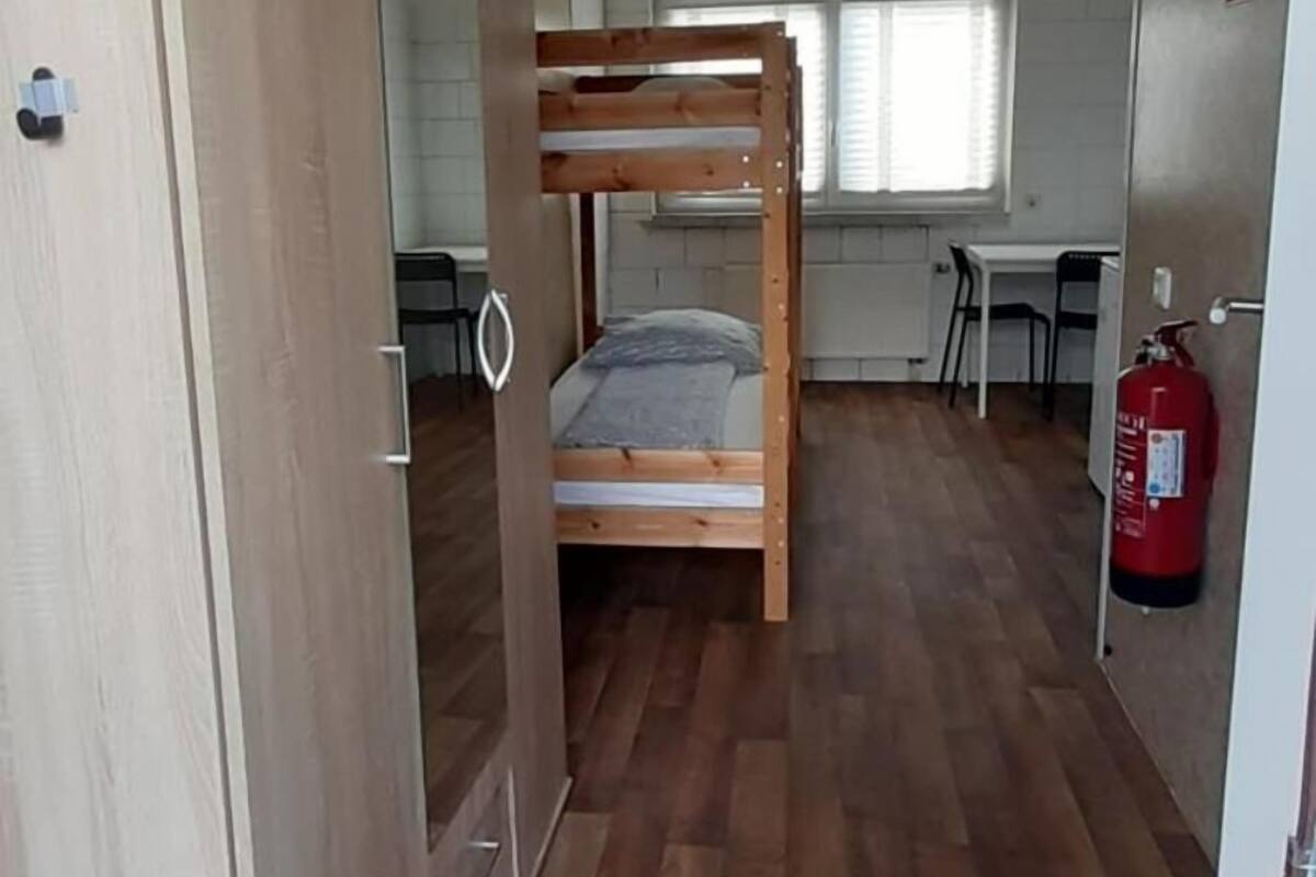 Une chambre avec un lit superposé, une armoire en bois et un extincteur.