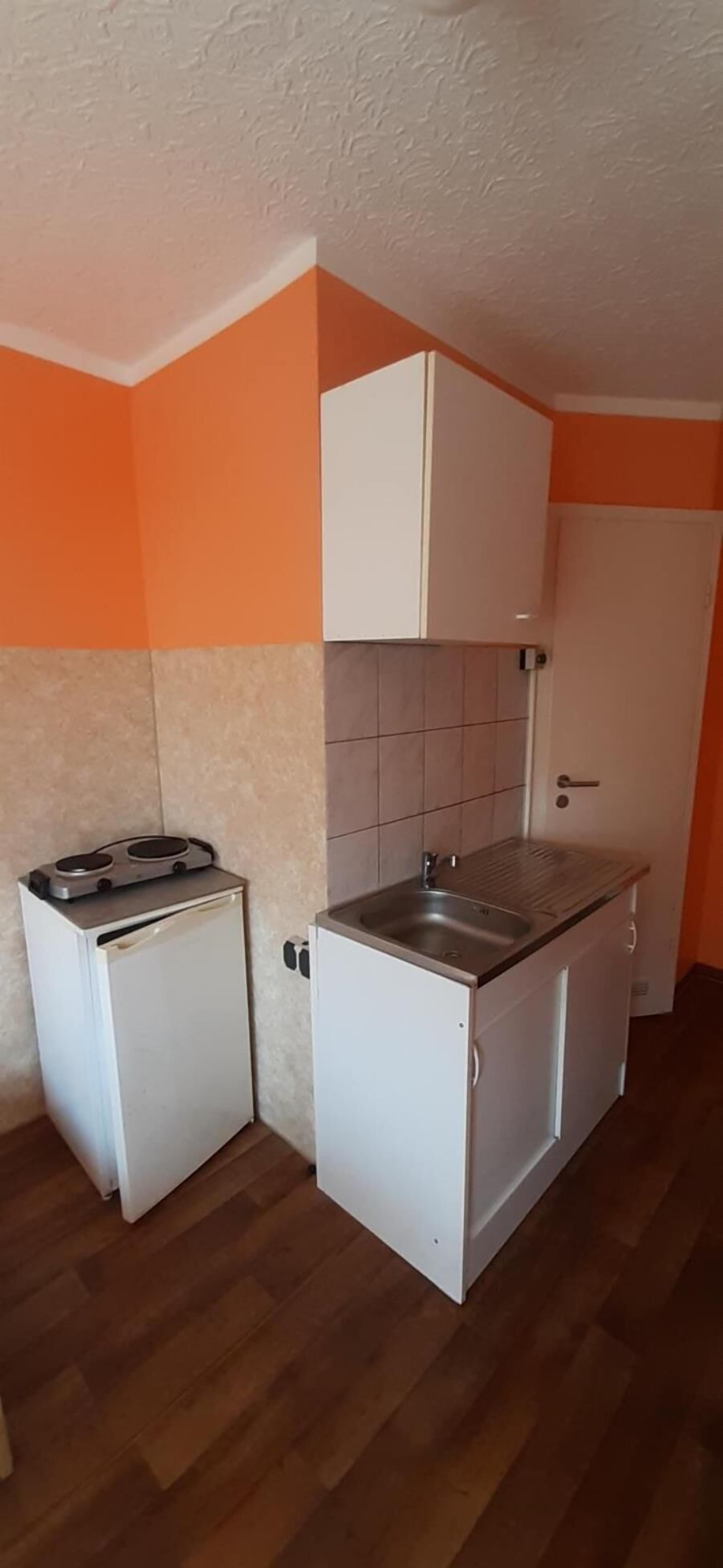 Une cuisine de taille réduite, équipée d’un réfrigérateur, d’une cuisinière, d’un évier et de meubles blancs.