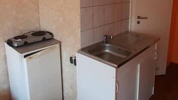 Une cuisine de taille réduite, équipée d’un réfrigérateur, d’une cuisinière, d’un évier et de meubles blancs.