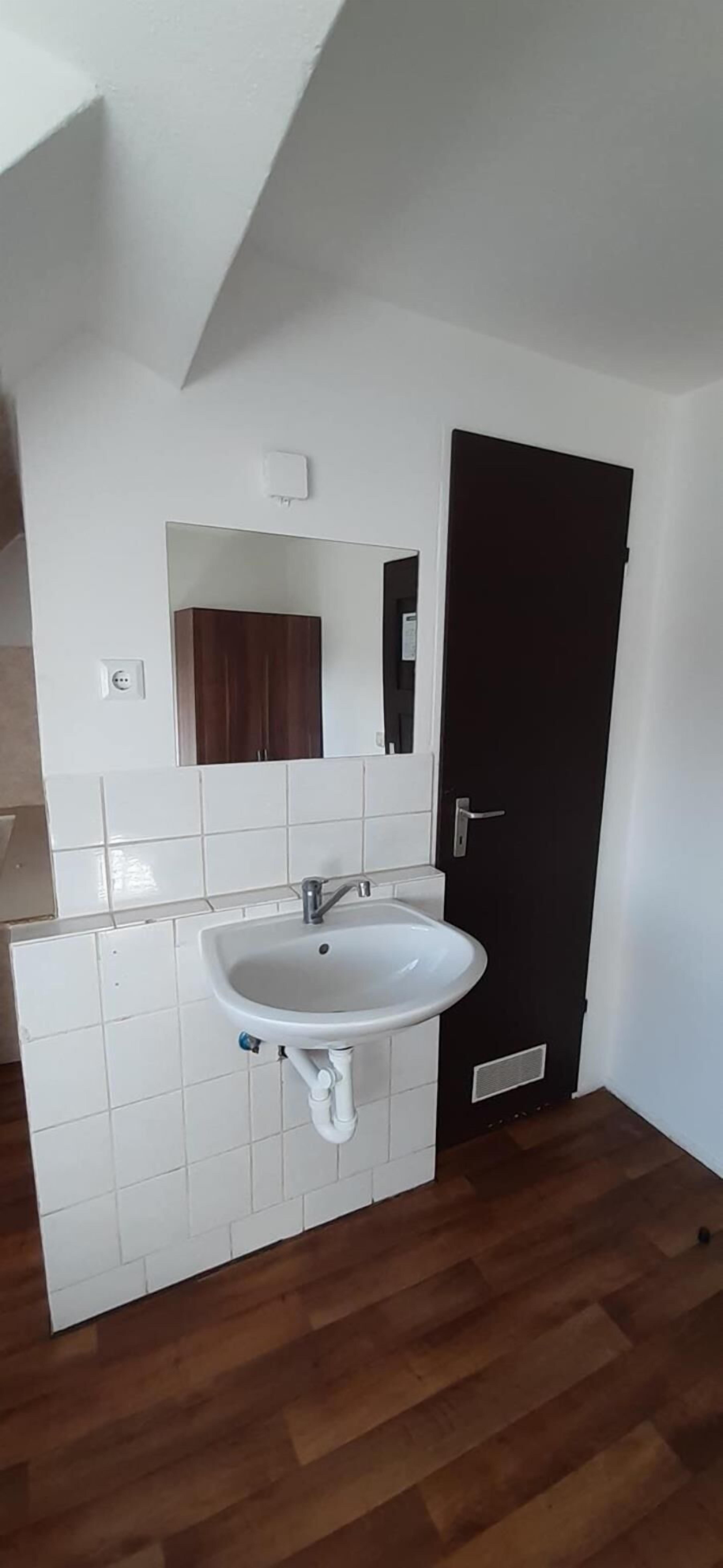 Une salle de bain avec un lavabo blanc, une porte sombre et un miroir au-dessus du lavabo.