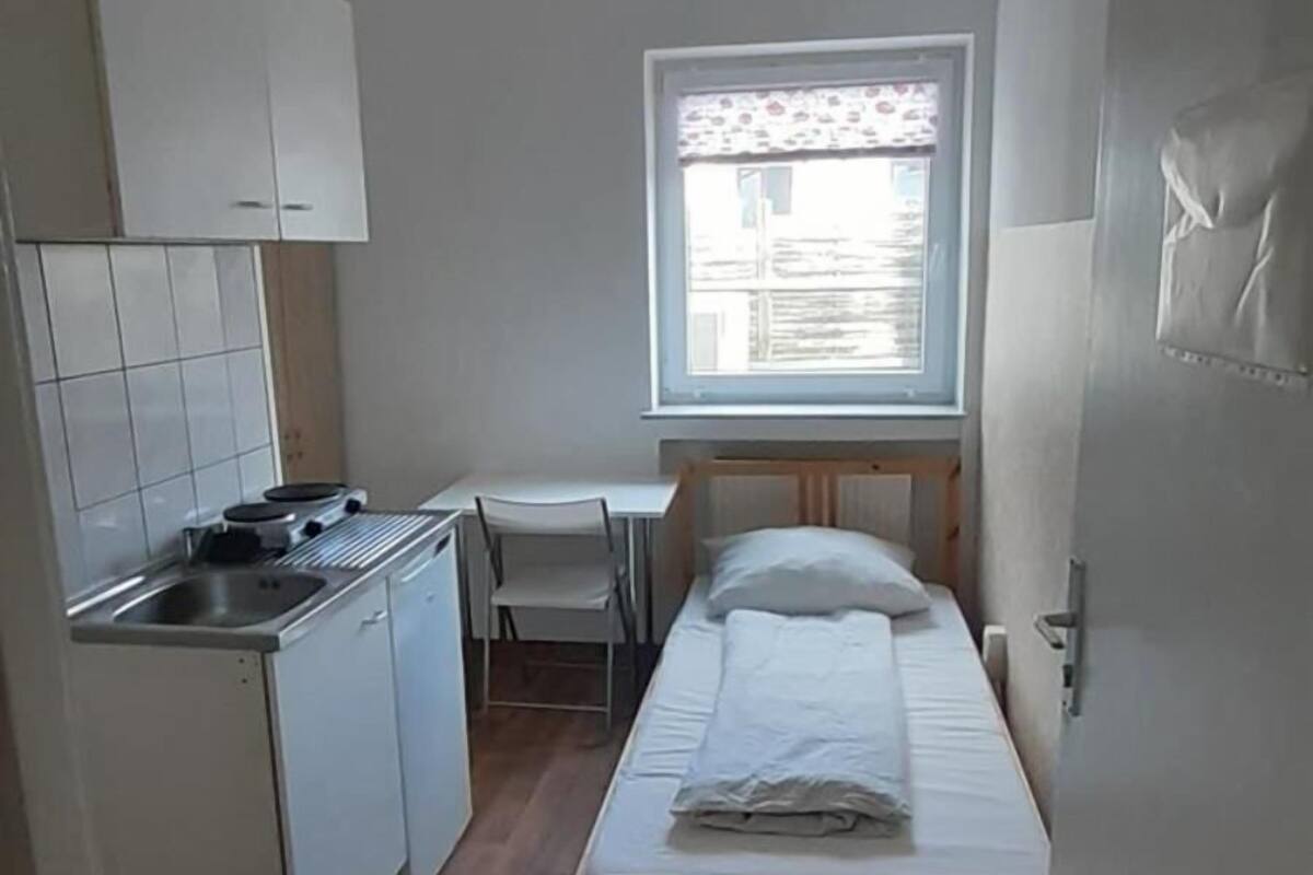 Une pièce de taille modeste comprenant un lit, un petit bureau et une kitchenette.