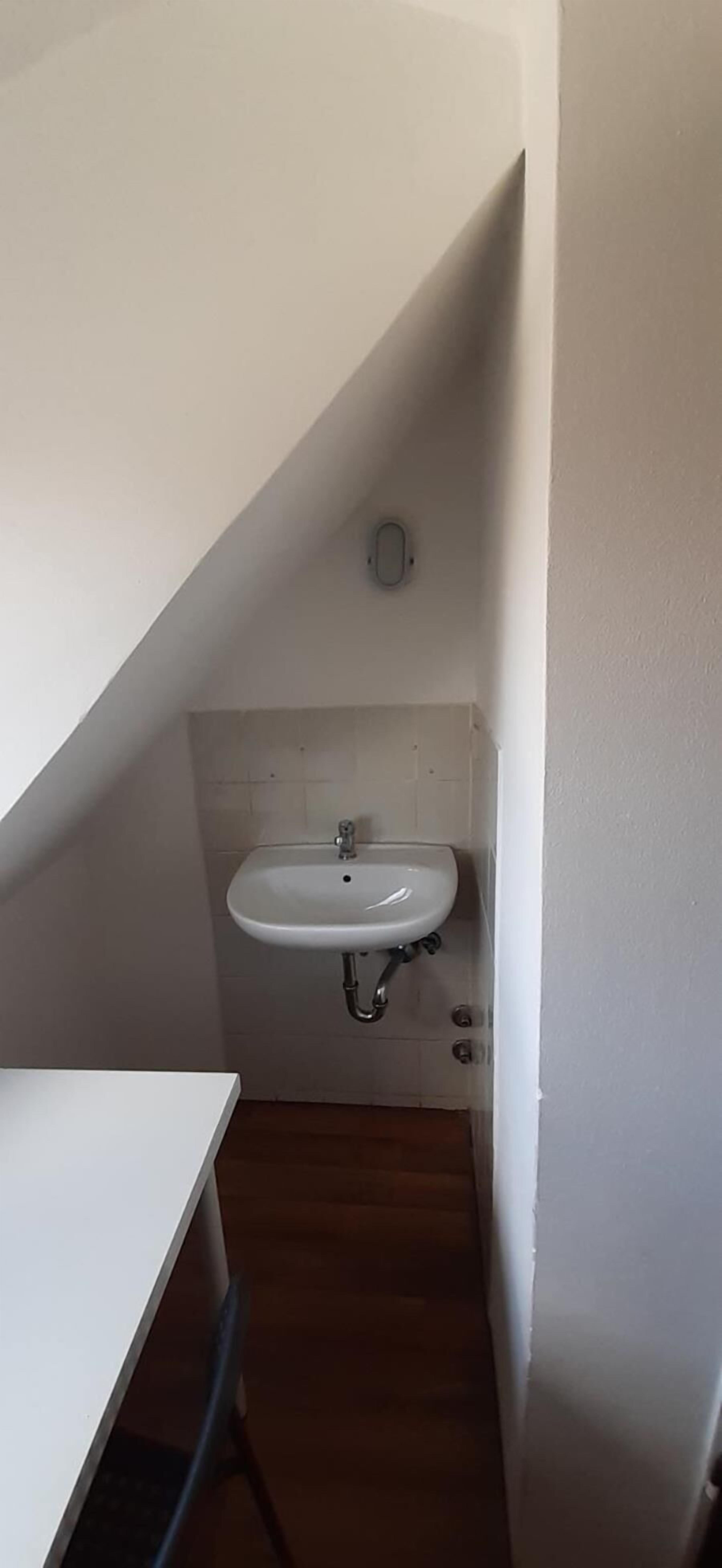 Un baño pequeño con un lavamanos blanco, un espejo y un perchero para toallas.