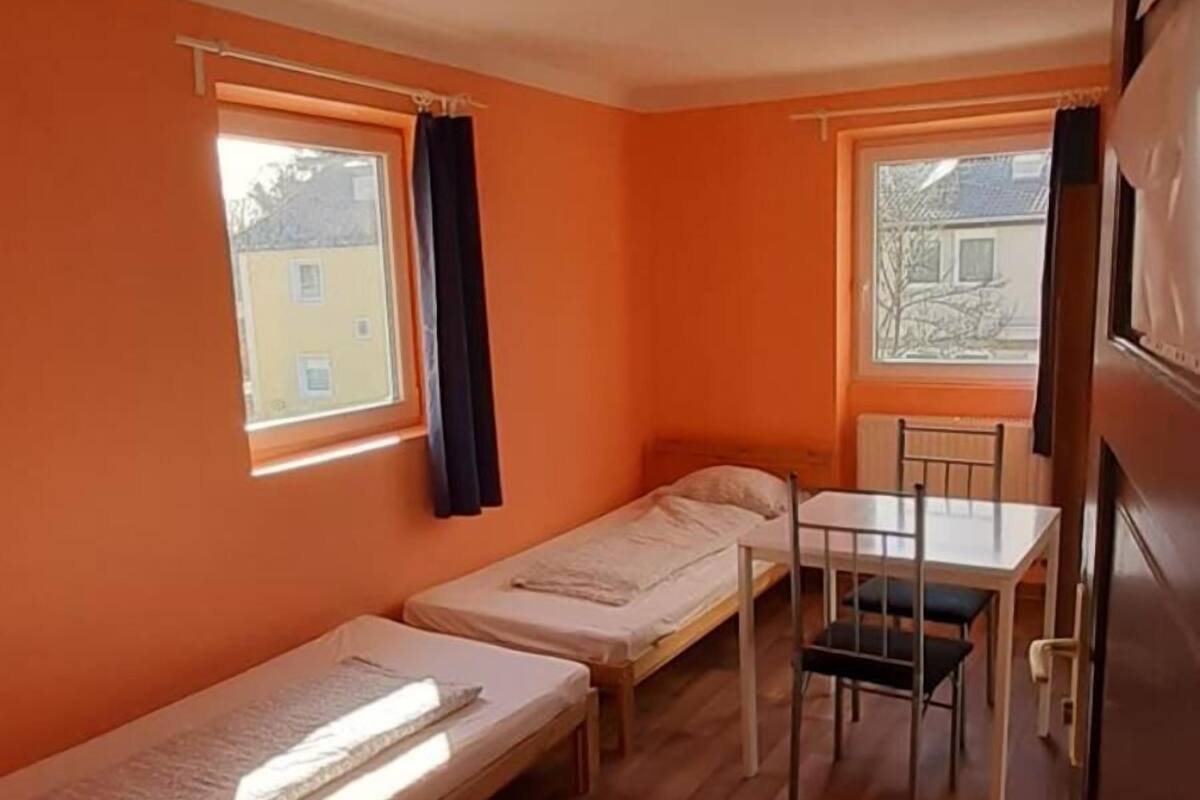Une chambre compacte comprenant deux lits simples, une petite table avec une chaise et une fenêtre laissant entrer la lumière naturelle.