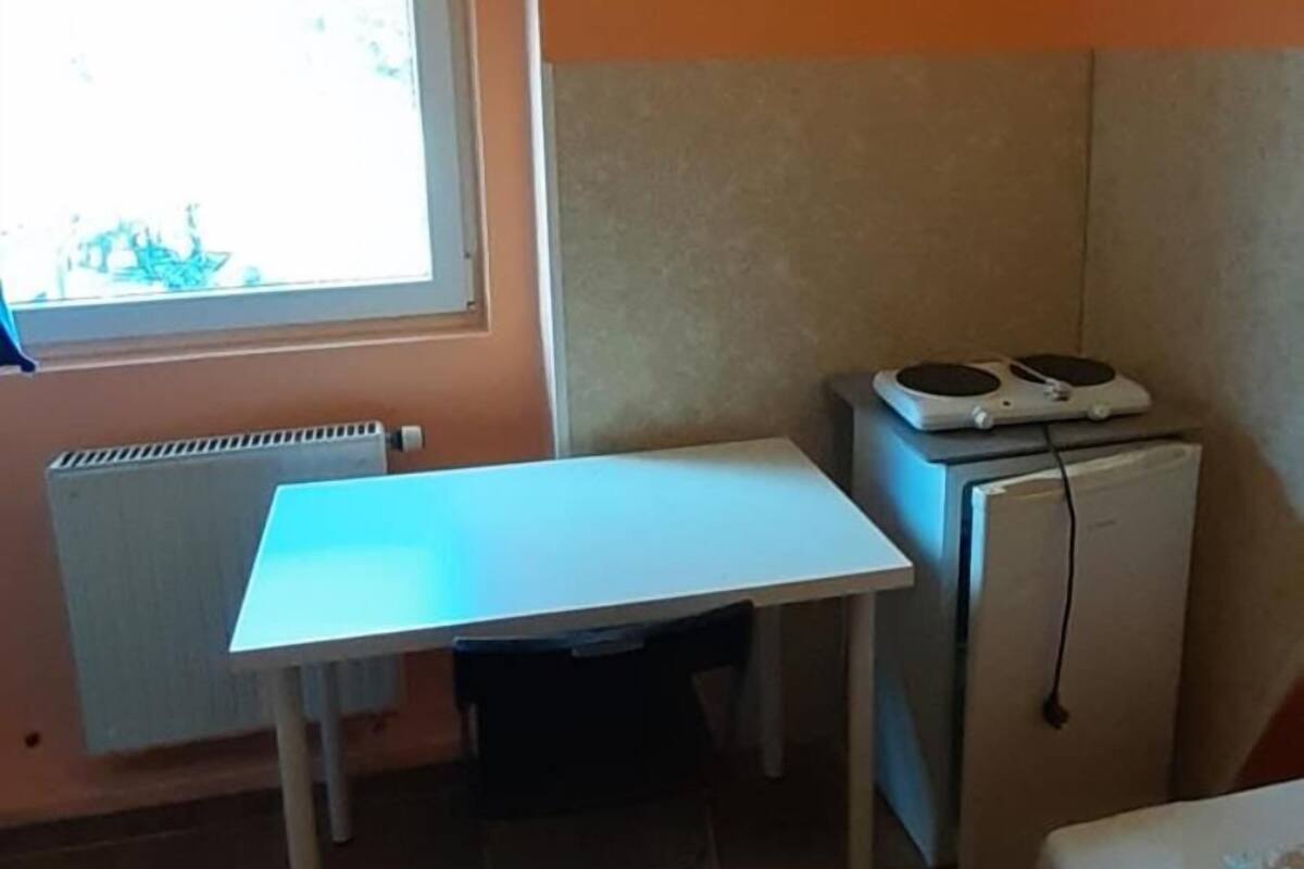 Une petite pièce avec une table blanche, un petit réfrigérateur, une fenêtre donnant sur un paysage agréable et un radiateur.