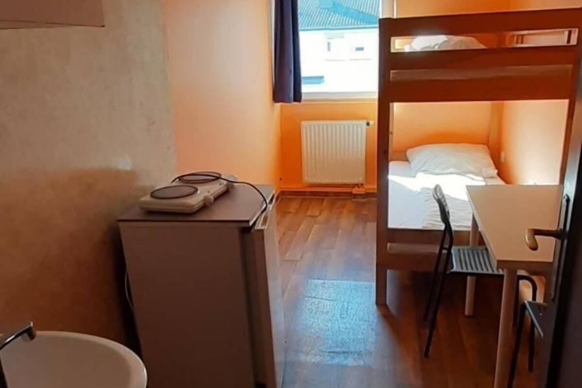 Une petite pièce comprenant un lit superposé, un coin cuisine, un évier et une fenêtre avec des rideaux.