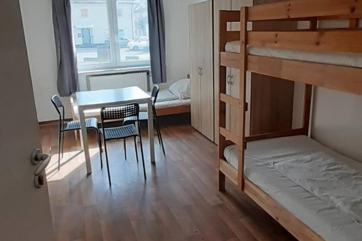 Une chambre avec un lit superposé, une table avec des chaises et une fenêtre avec des rideaux.