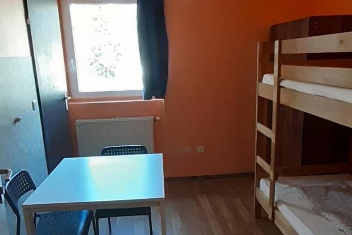 Une chambre avec un lit superposé, une table avec des chaises, une fenêtre avec des rideaux et un ventilateur de plafond.