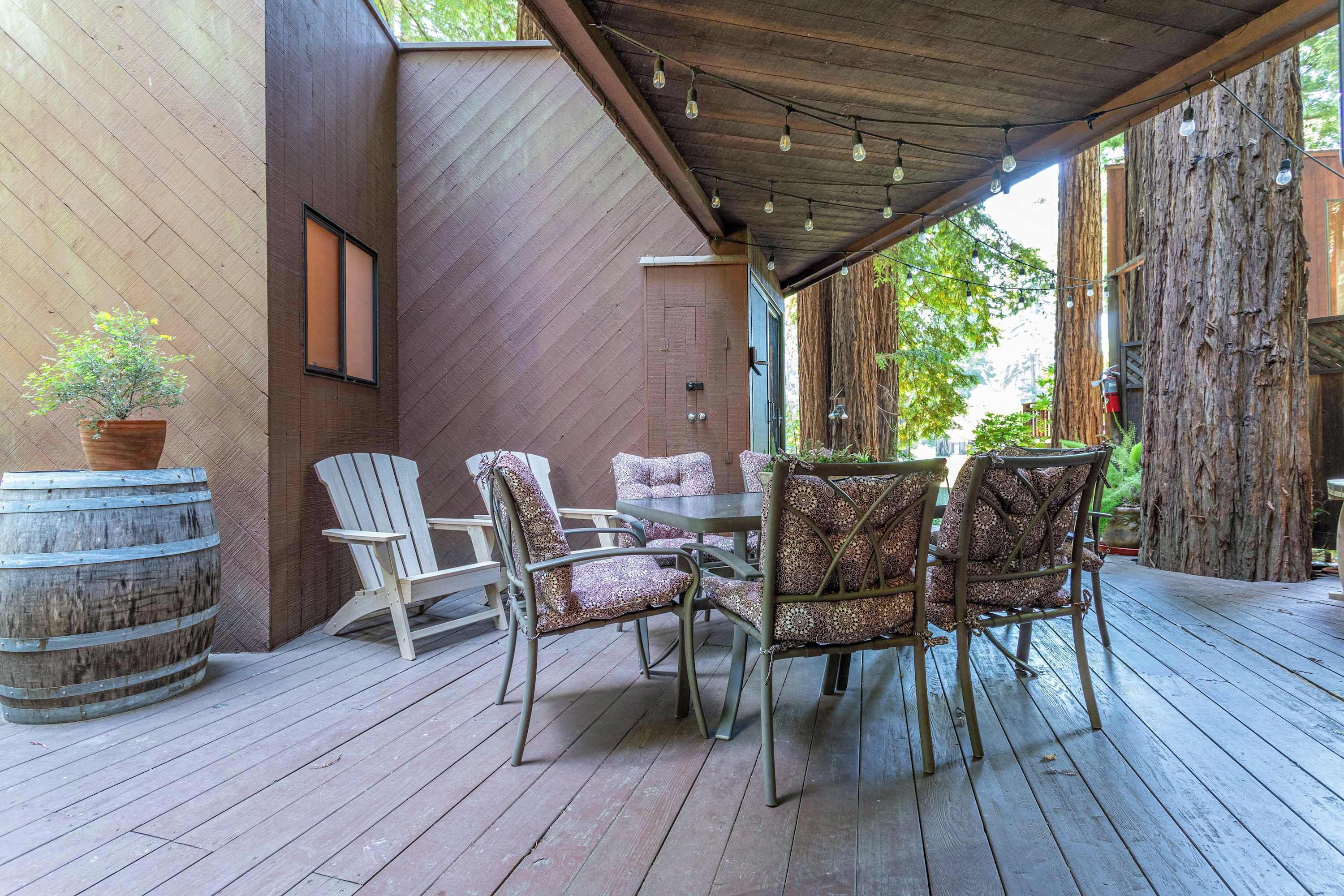 An outdoor patio with a wooden deck, metal chairs, a round table, and a large barrel.