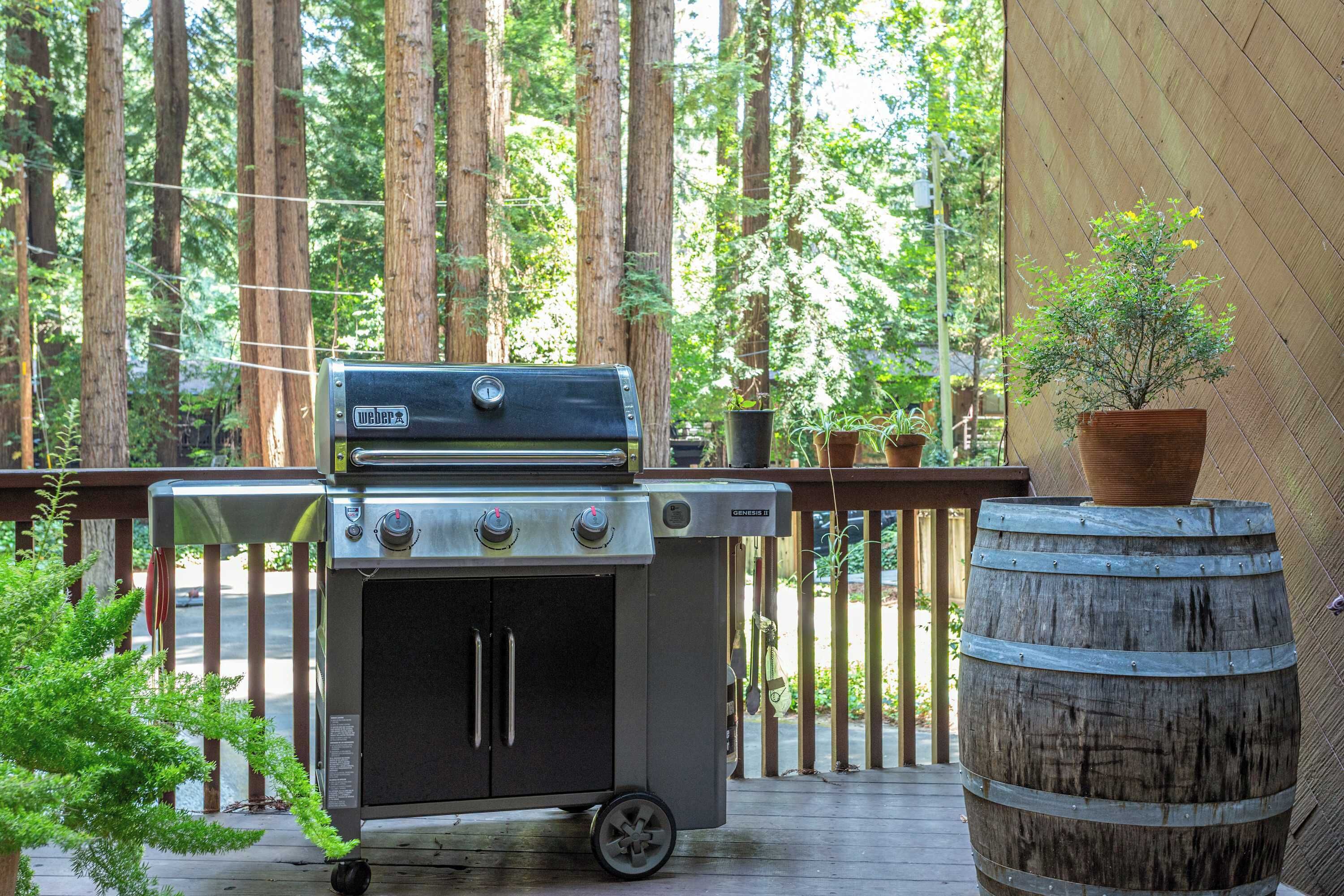 A portable barbecue grill on a wooden deck with a view of tall trees in the background.