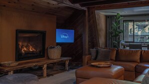 A cozy living room with a fireplace, leather sofa, and a television displaying Disney+. - Tri-Level MCM Masterpiece, Redwoods, Golf & Spa (Monte Rio)