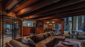 A spacious living area with a leather sectional sofa, a wooden coffee table, and a dining area with chairs and a table. - Tri-Level MCM Masterpiece, Redwoods, Golf & Spa (Monte Rio)