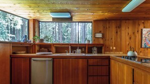 A wooden cabin kitchen with a built-in dishwasher, a large window overlooking a forest, and a rustic decor. - Tri-Level MCM Masterpiece, Redwoods, Golf & Spa (Monte Rio)