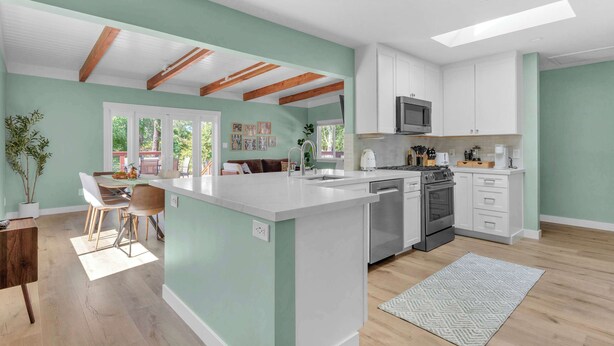 A modern kitchen with white cabinetry, a central island, and a dining area with a table and chairs. - Modern Country Home | Near Downtown & Bike Trail (Sebastopol)