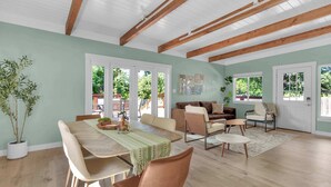 A spacious living area with a dining table, chairs, a sofa, and a coffee table. There are large windows allowing natural light and views of greenery outside. - Modern Country Home | Near Downtown & Bike Trail (Sebastopol)