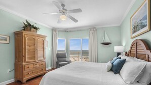 Un dormitorio con una cama grande, un armario de madera, un ventilador de techo y vistas a la playa desde la ventana.