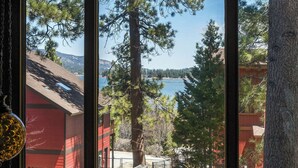 Vista a través de una ventana de un edificio de fachada roja, una valla de madera y un lago con árboles al fondo.