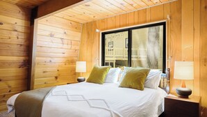 Un dormitorio con paneles de madera, un ventanal grande, una cama con ropa de cama blanca y dos lámparas de noche.