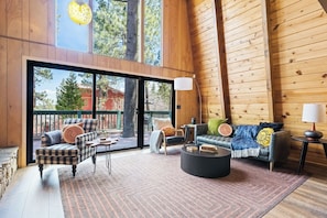 A spacious living area with a large sliding glass door leading to an outdoor deck, furnished with a sofa, armchairs, and a coffee table.
