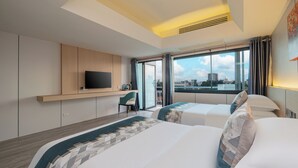 Ein modernes Hotelzimmer mit zwei Betten, einem Fernseher, einem Schreibtisch und Blick auf die Stadt.