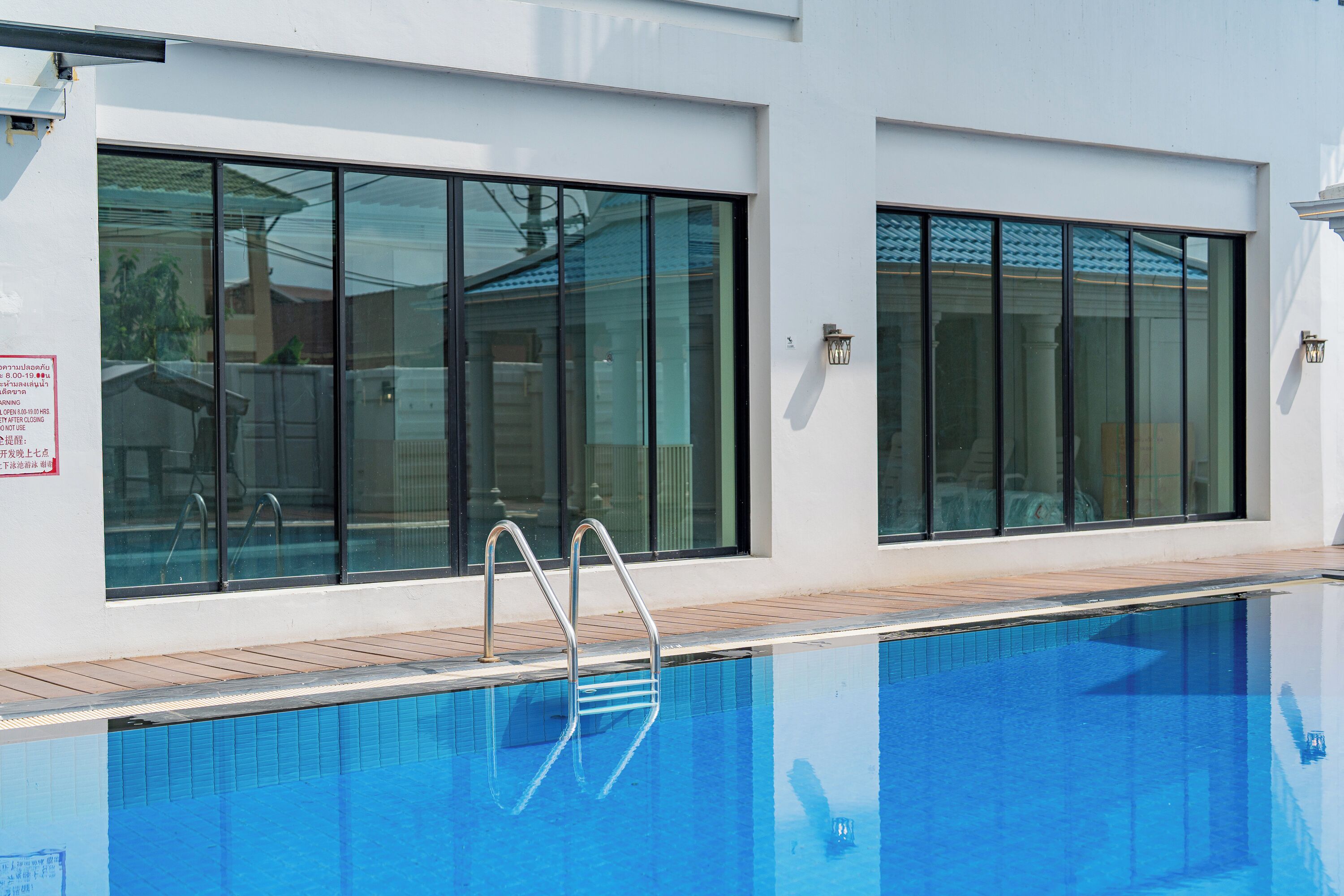 A swimming pool with a clear blue water surface, adjacent to a building with large windows and a wooden deck.