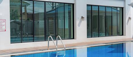A swimming pool with a clear blue water surface, adjacent to a building with large windows and a wooden deck.