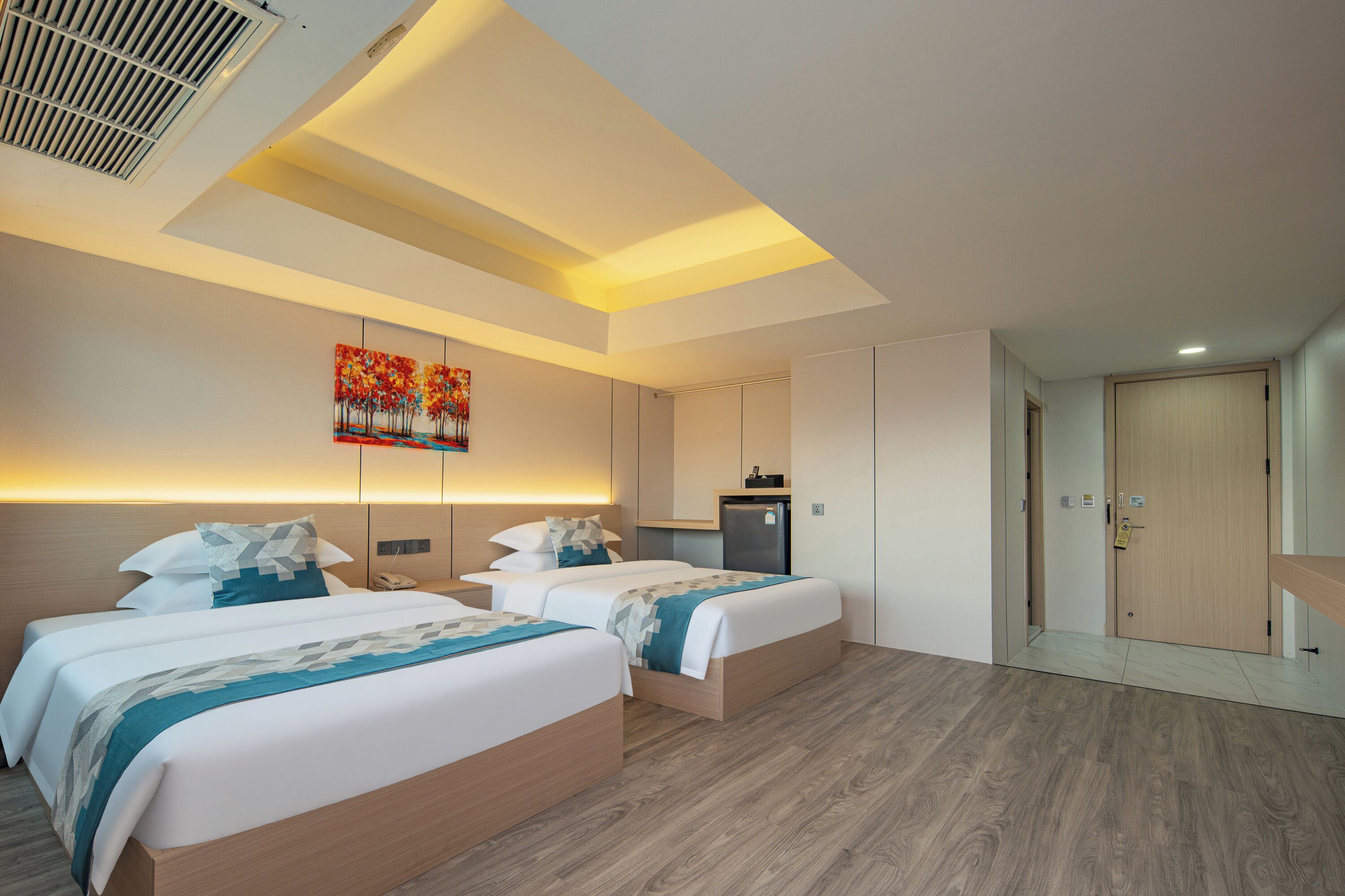 A modern hotel room with two beds, a small kitchenette, and a bathroom.