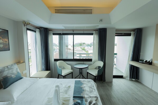 A hotel room with a bed, two chairs, a small table, and a window with curtains. - Xinmylin Boutique Resort Hotel (Pattaya)