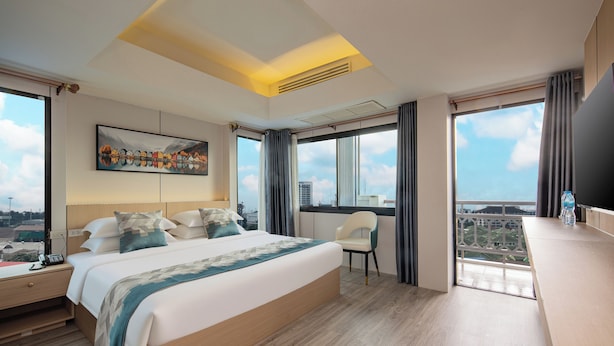 Ein modernes Hotelzimmer mit einem großen Bett, einem Schreibtisch mit Telefon, einem Sessel und einem Fernseher.