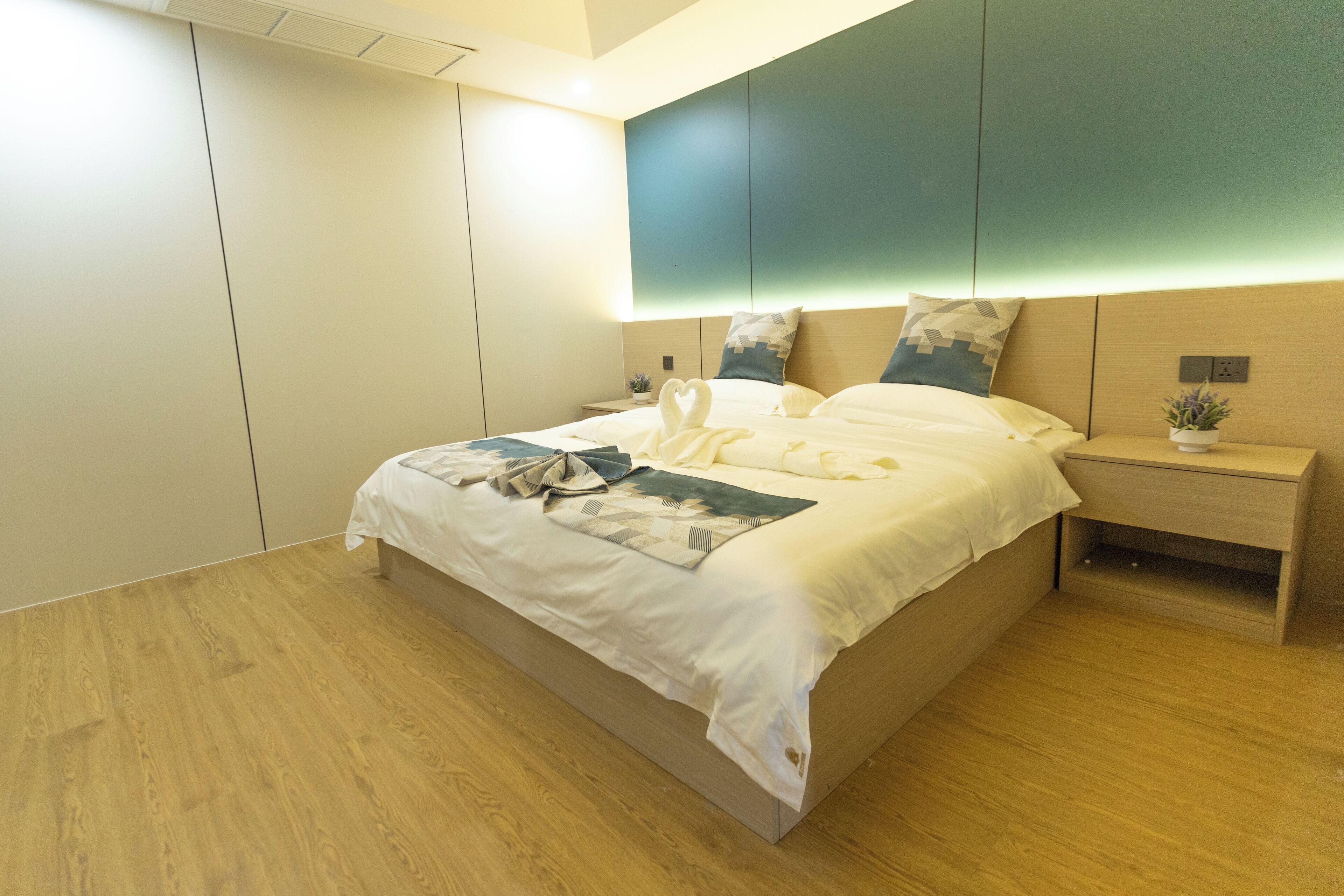 A modern bedroom with a large bed, a bedside table with a plant, and a wall-mounted light.