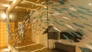 Ein modernes Interieur mit einer Glaswand, die Fischskulpturen zeigt, einer Treppe und einem gerahmten Foto auf dem Boden.