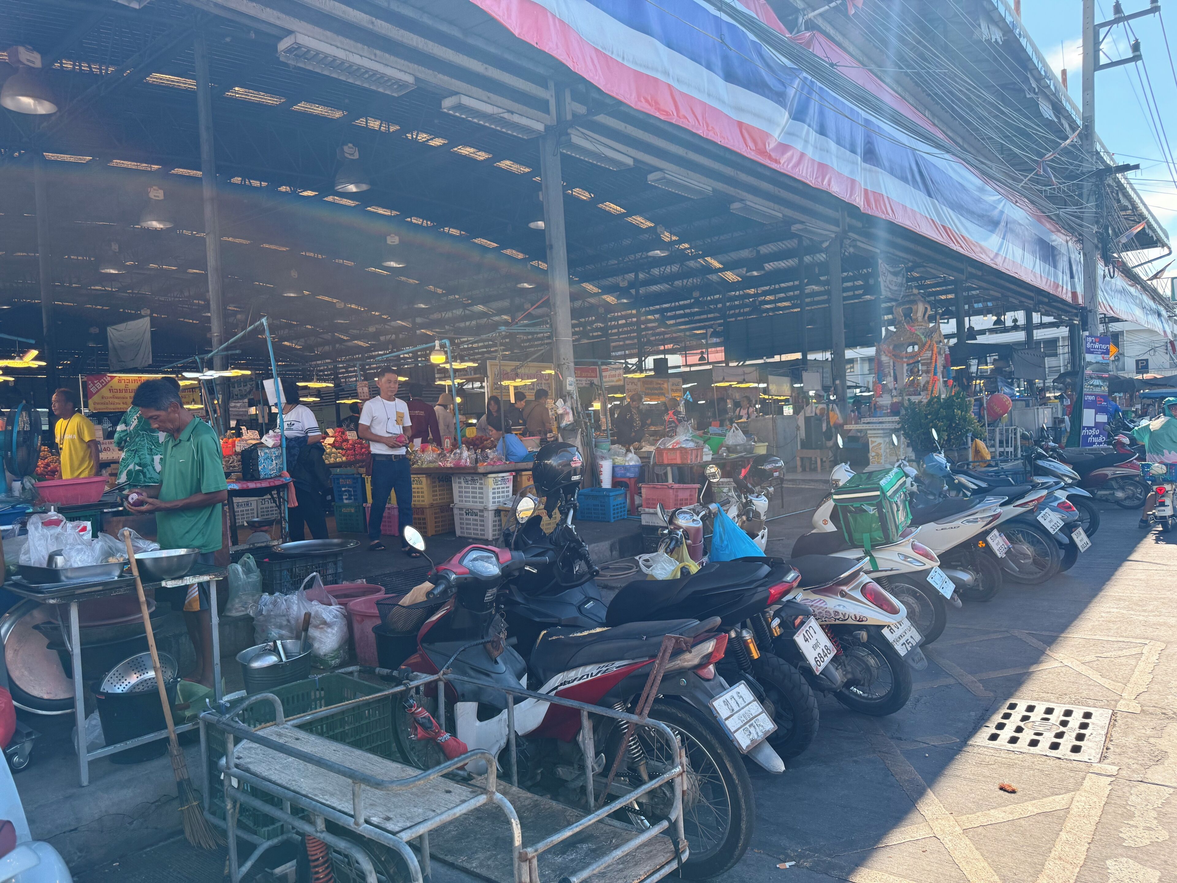 A market with various stalls, a covered area, and motorcycles parked along the side.