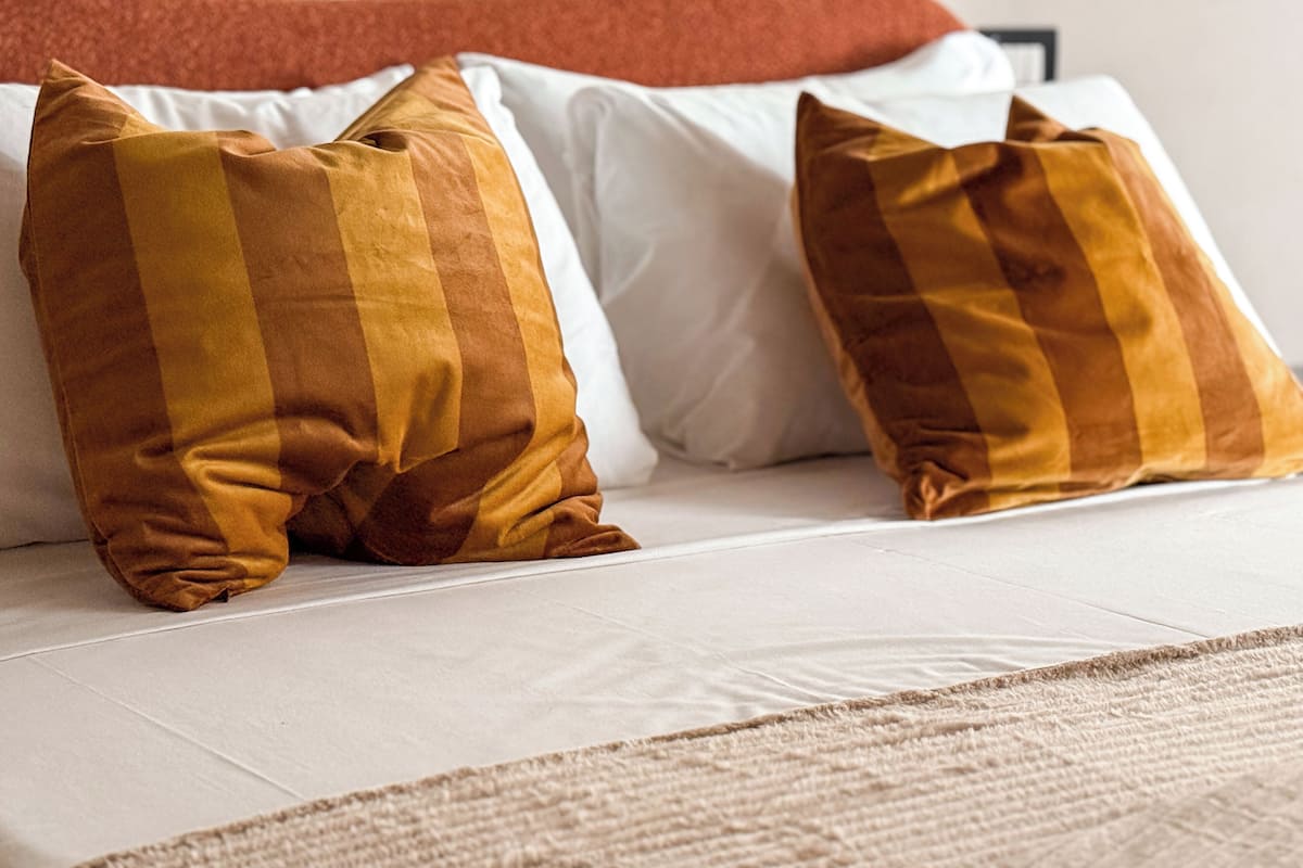 A bed with two pillows, one striped in shades of brown and the other plain white.