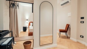 A modern hotel room with a large mirror, a piano, a wicker basket, and a chair. - The Rubens Spagna (Rome)