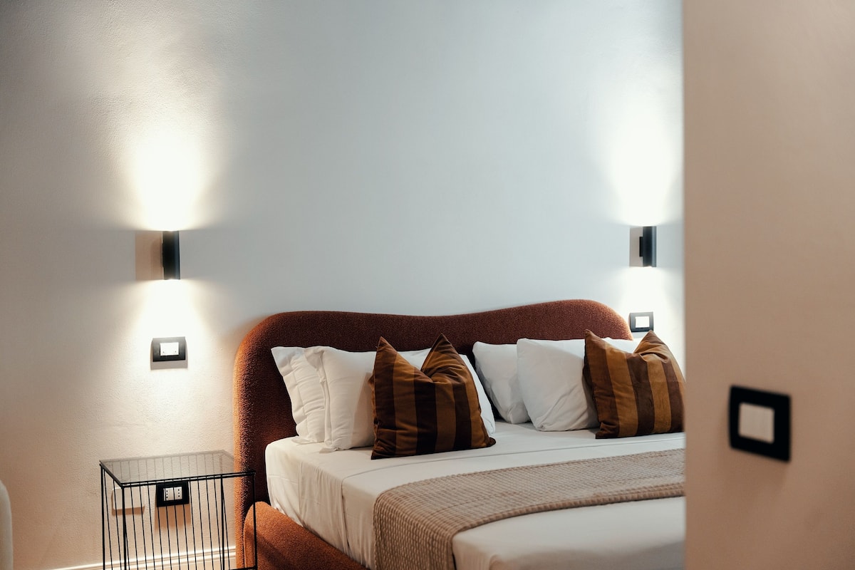 A neatly made bed with white and brown pillows, a brown headboard, and two wall-mounted light fixtures.