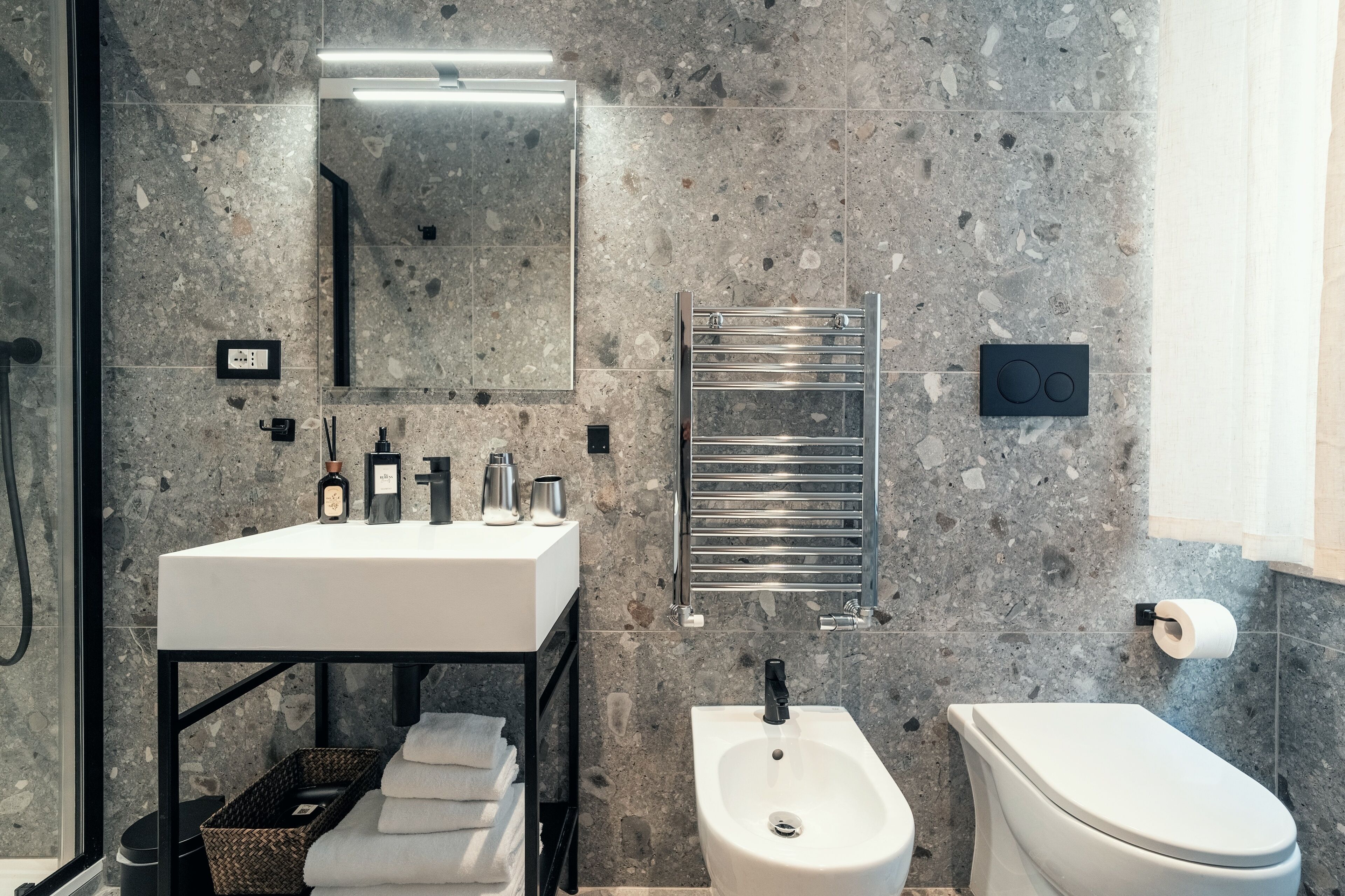 A modern bathroom with a white sink, bidet, and toilet, marble walls, and a towel rack.