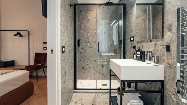 A modern bathroom with a glass-enclosed shower, a white sink, and a towel rack. - The Rubens Spagna (Rome)