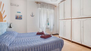 Un dormitorio con cama, armario, mesita de noche, lámpara, un cuadro y un cartel.