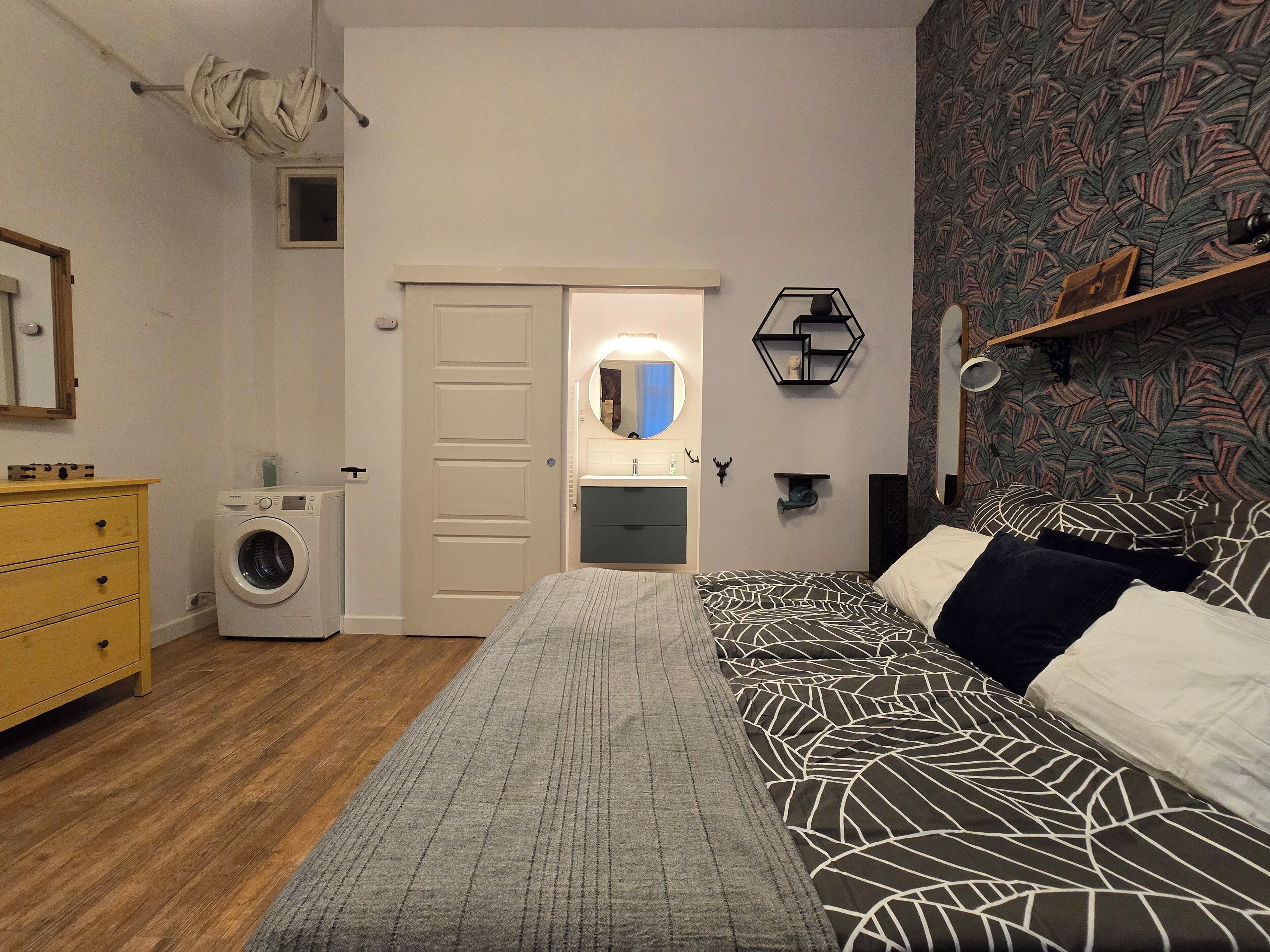 Une chambre à coucher avec un lit, une machine à laver, une commode et un miroir.