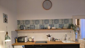 A compact kitchen with a microwave, kettle, and coffee maker on the counter, a sink, and a clock on the wall.