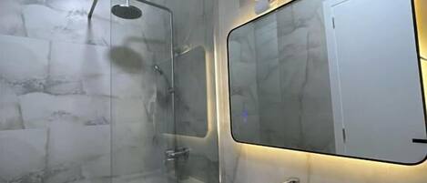 A modern bathroom with a glass-enclosed shower, a marble sink, and a mirror with integrated lighting.