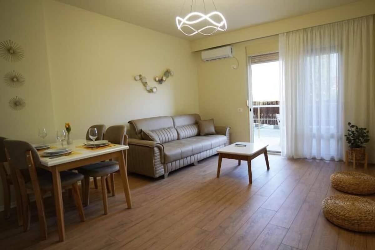 Ein Wohnzimmer mit einer Couch, einem Esstisch mit Stühlen, einem Couchtisch und einem an der Wand befestigten Fernseher.