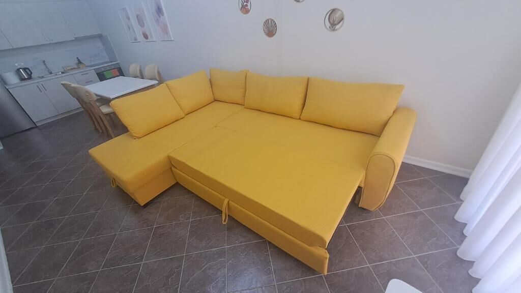 A yellow sectional sofa in a living room with a kitchen area visible in the background.
